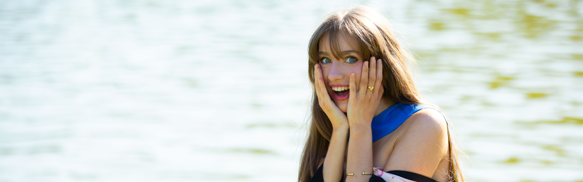 UCD alumna posing by the main lake at her graduation with her head in her hands, amused look on her face.